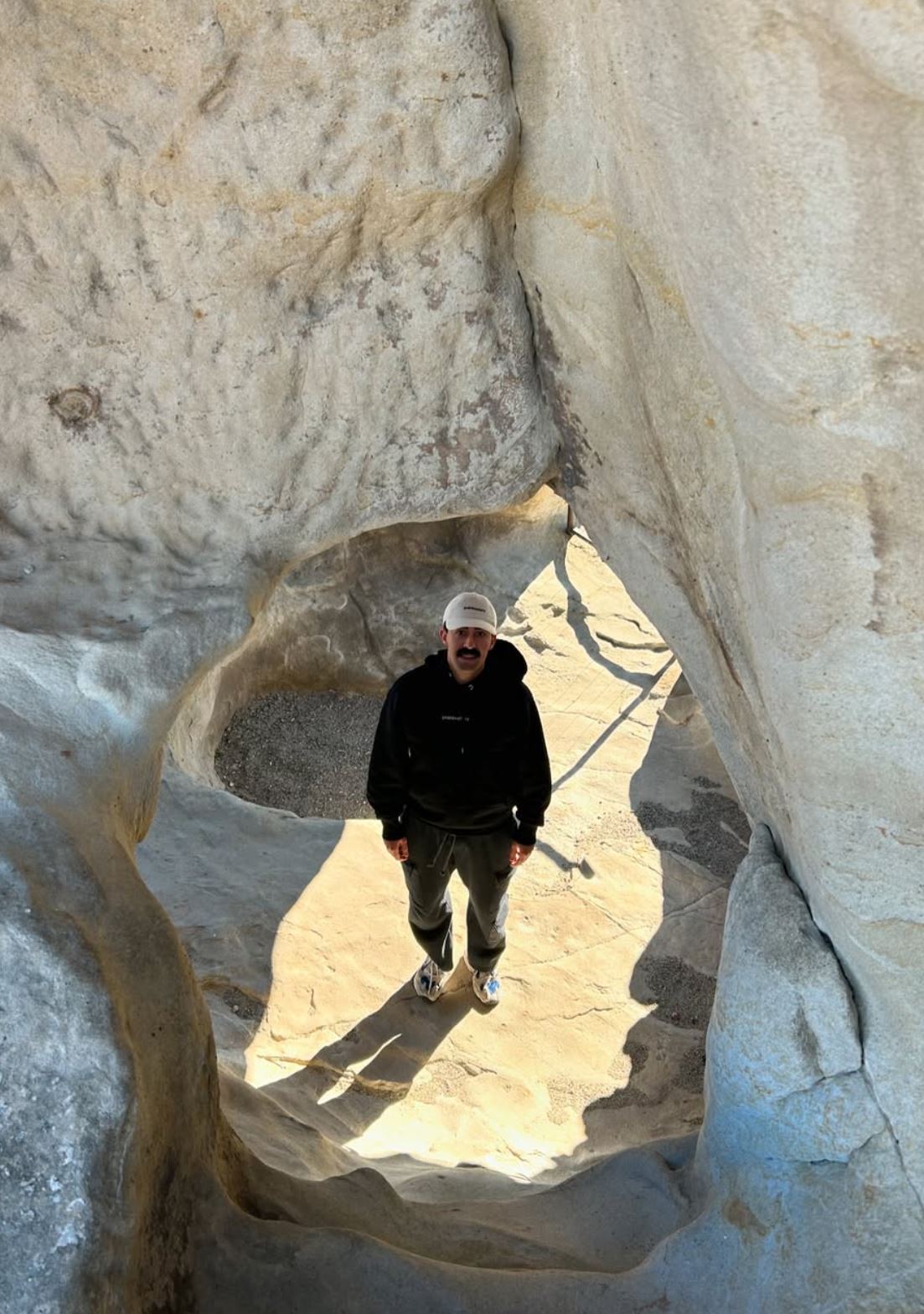 Mory Naimi wearing full Painbusterz gear, black hoodie and cream hat, in the mountains.