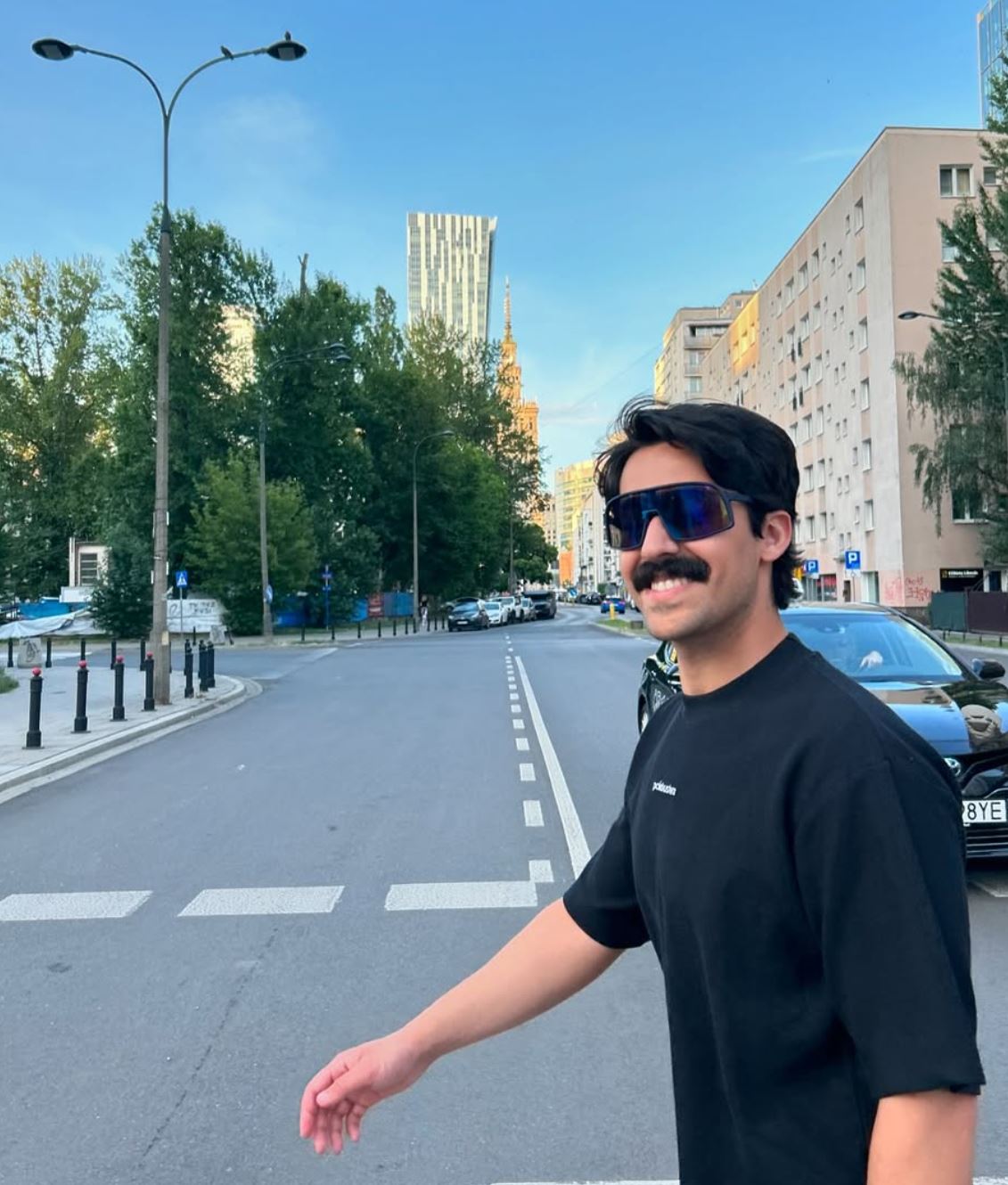 Mory Naimi wearing a black Painbusterz T-shirt and sunglasses walking in the city.