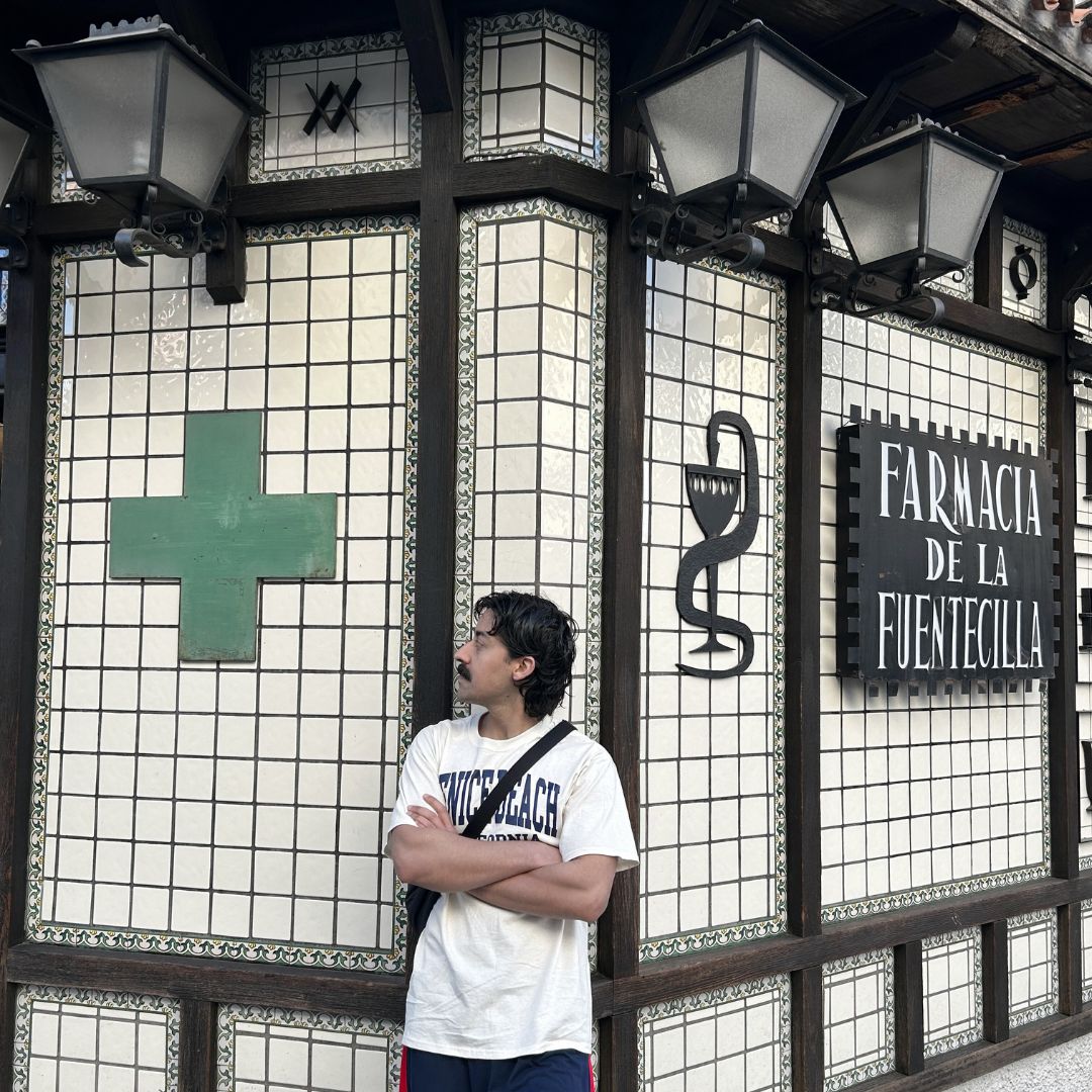 Mory Naimi in Spain looking at a pharmacy cross sign and a snake symbol nearby, part of a Painbusterz Instagram post exploring the mythology of snakes and medical symbols.